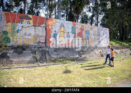 Two tourist hikers standing and admiring a colorful Soviet-era mosaic on a rustic concrete public bus stop in the rural countryside of Georgia. Stock Photo