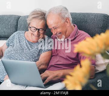 Aged old senior couple using together a laptop sitting on the sofa surfing the web. Looking for on web internet pages concept activity with mature man Stock Photo