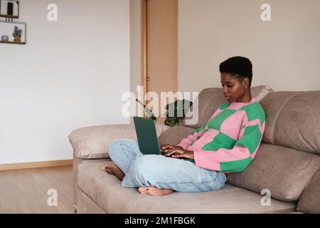 Black female freelancer using laptop while sitting on sofa Stock Photo