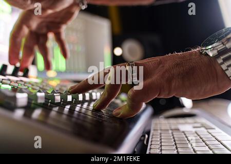 Close-up of caucasian music producer fading volume on sound mixer control panel in small music production studio - audio engineer at work - music and Stock Photo