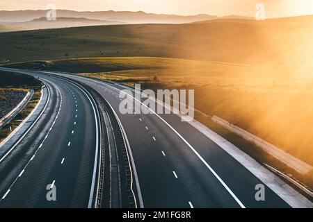 Sunset on a highway with surrounding mountains Stock Photo