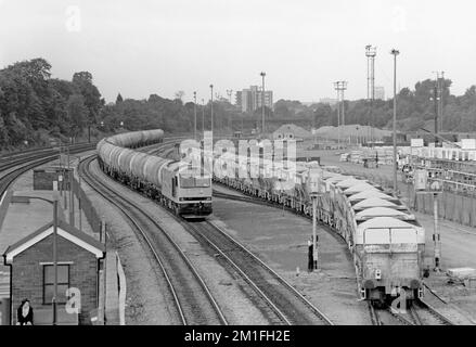 A Class 60 diesel locomotive number  60056 with a train of bogie oil tanks waits time in Acton Yard as a train of loaded PGA stone hoppers enters the yard. Acton Main Line. 10th June 1991. Stock Photo