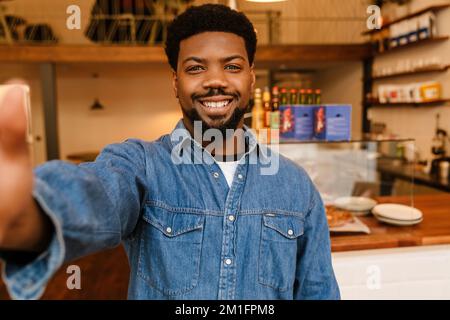 Black bearded man smiling while taking selfie photo in cafe indoors Stock Photo