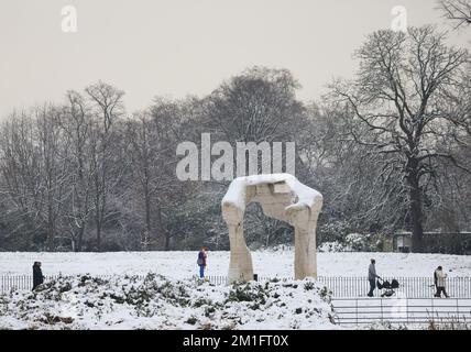 People walk through the snow by the six-metre high Roman travertine sculpture, The Arch, by artist Henry Moore in Hyde Park, central London. Snow and ice have swept across parts of the UK, with cold wintry conditions set to continue for days.. Picture date: Monday December 12, 2022. Credit: Isabel Infantes/Alamy Live News Stock Photo