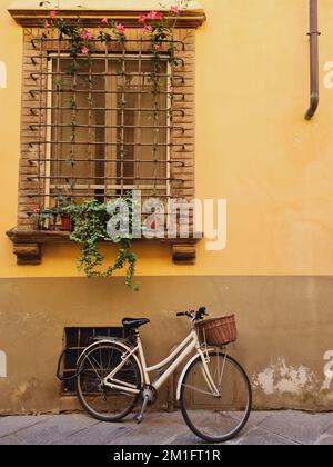 A white bicycle parked next to a yellow building under a fenced window Stock Photo