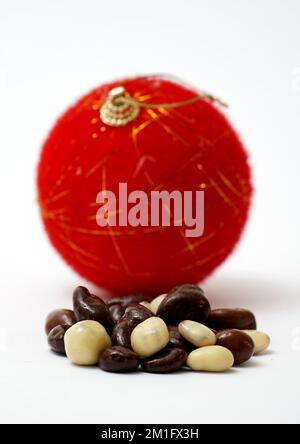 crunchy milk chocolate sweets in front of red christmas bauble on white background. Stock Photo