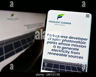 Person holding smartphone with website and logo of Portuguese energy company Frequent Summer S.A. on screen. Focus on center of phone display. Stock Photo