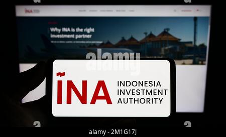 Person holding smartphone with logo of Indonesia Investment Authority (INA) on screen in front of website. Focus on phone display. Stock Photo