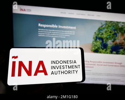 Person holding cellphone with logo of Indonesia Investment Authority (INA) on screen in front of business webpage. Focus on phone display. Stock Photo
