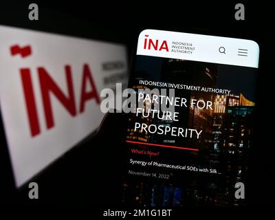 Person holding cellphone with website of Indonesia Investment Authority (INA) on screen in front of logo. Focus on center of phone display. Stock Photo