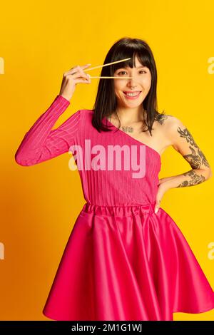 Young smiling girl with tattoos in bright pink clothes posing isolated on vivid yellow background. Concept of youth, beauty, fashion, lifestyle Stock Photo