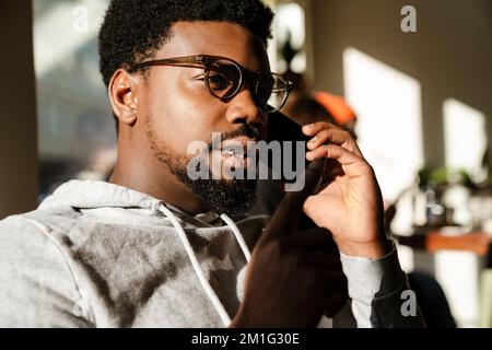 Black bearded man talking on mobile phone and gesturing in cafe indoors Stock Photo