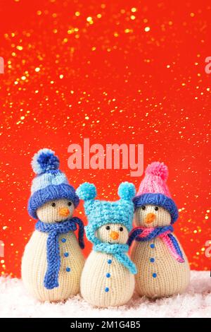 Three knitted snowmen on a red background in blue and pink hats. Merry Christmas and New Year 2023 greeting card Stock Photo