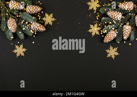 Green branches of a Christmas tree with decorations in the form of golden cones and snowflakes on a black background with twinkling festive lights wit Stock Photo