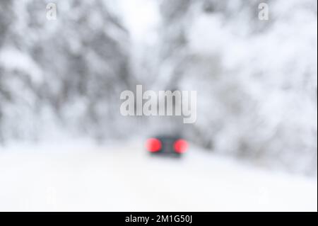 Blurred abstract snow covered trees in forest and red car tail lights on the road Stock Photo