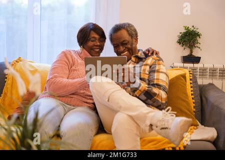 Senior couple together on the sofa using the tablet and communicating with their family online Stock Photo