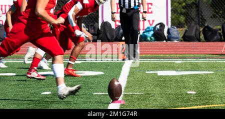 A football team in red uniforms running toward the ball on a tee for the kickoff on a green turf field. Stock Photo