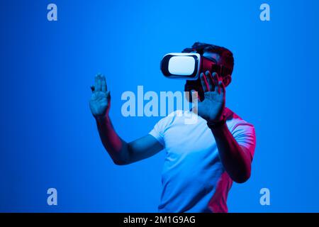 Bearded brunette man in white t-shirt wearing virtual reality goggle and immersing himself in VR multimedia. Future technology concept. Stock Photo
