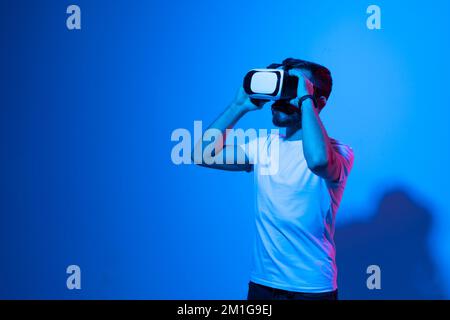Portrait of young man with 3D virtual reality glasses enjoys his trip in an adventurous world in neon light. Concept of connection technology with Stock Photo