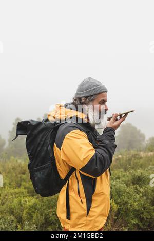 A man picks up the signal on his mobile phone and sends a voice message, Hiker with backpack talking on the cell phone during an excursion Stock Photo