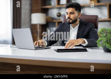 Focus on hands confident businessman wearing suit writing notes or financial report, sitting at desk with laptop, focused serious man working with paper documents student studying online research work Stock Photo