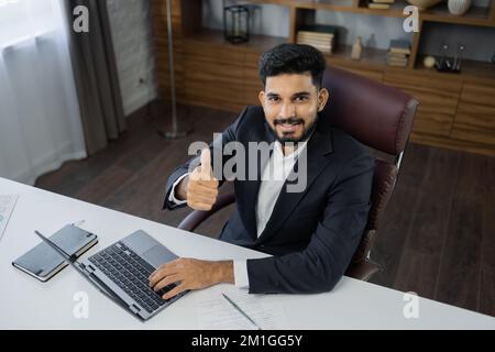 High angle view of stylish bearded businessman works on laptop, data analysis and creative designer, looking at computer showing thumb up. Digital entrepreneur working on e-commerce startup project Stock Photo