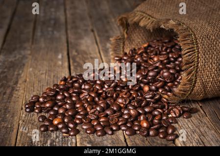 Sack of coffee beans overturned on an old rustic table with the beans scattered on top. Stock Photo