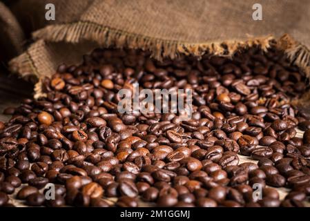 Sack of coffee beans overturned on an old rustic table with the beans scattered on top. Stock Photo
