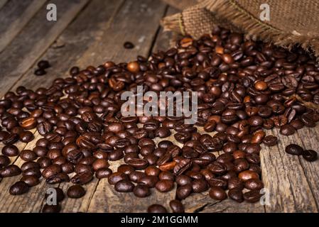 Sack of coffee beans overturned on an old rustic table with the beans scattered on top. Stock Photo