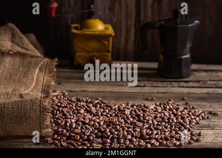 Roasted coffee beans coming out of a sack on a wooden table and in the background an old coffee grinder. Stock Photo