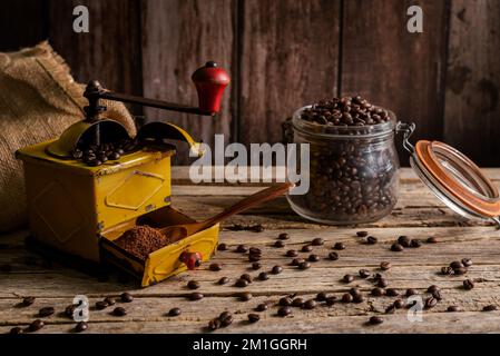 Old coffee grinder with beans and freshly ground coffee, next to a pot with roasted coffee beans. Stock Photo