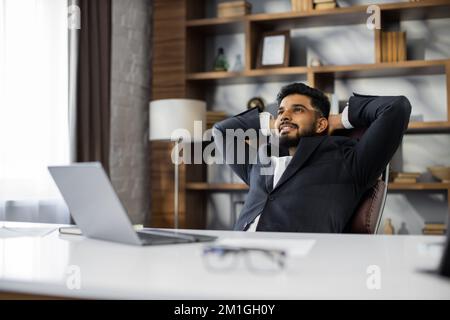 Confident man in glasses sitting relax at home office workplace take nap or daydream. Happy relaxed Caucasian young male rest in chair distracted from computer work, relieve negative emotions. Stock Photo