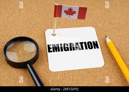 On the table is the flag of Canada, a pencil, a magnifying glass and a sheet of paper with the inscription - Emigration. Stock Photo