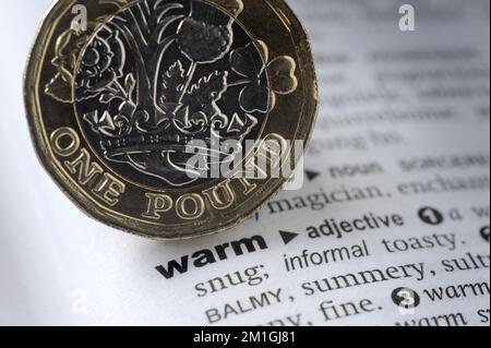 DICTIONARY DEFINITION OF WORD WARM WITH ONE POUND COIN RE COST OF LIVING CRISIS HEATING HOMES FUEL COSTS ETC UK Stock Photo