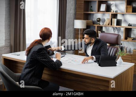 Businessman conducting an employment interview with an attractive young female applicant sitting opposite him at the desk in the office answering his question concerning her CV Stock Photo