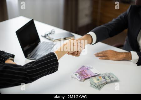 Close up of business partners handshake deal come to agreement. Businesswoman offering batch of hundred dollar bills and euros to male ceo in modern office. Stock Photo