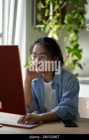 Focused Asian girl freelance software developer in eyeglasses working on computer at home Stock Photo