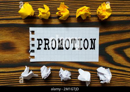 Business and finance concept. On a wooden board lie crumpled leaves of paper and a sheet from a notebook on which it is written - PROMOTION Stock Photo