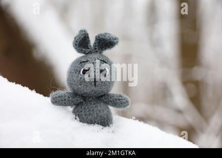 Grey knitted rabbit on a branch of snow covered tree. Symbol of Chinese New Year 2023 Stock Photo