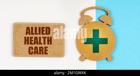 Medicine and health concept. On the white and blue surface are an alarm clock and a sign with the inscription - Allied Health Care Stock Photo