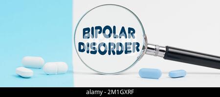 Medicine and health concept. On a blue and white background, there are pills and a magnifying glass, inside of which it is written - BIPOLAR DISORDER Stock Photo