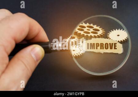 Business and finance concept. In his hand is a magnifying glass through which you can see the gears and scrap of paper with the inscription - IMPROVE Stock Photo