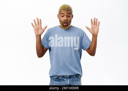 Portrait of surprised Black man raise hands up, drops smth and looks down with opened mouth, stands over white background Stock Photo