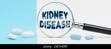 Medicine and health concept. On a blue and white background, there are pills and a magnifying glass, inside of which it is written - KIDNEY DISEASE Stock Photo