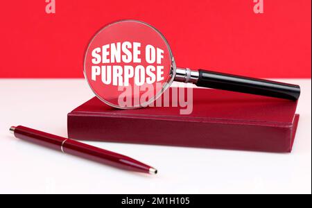 Business and finance concept. On a white and red background, a notebook, a pen and a magnifying glass, inside which the inscription - Sense of Purpose Stock Photo