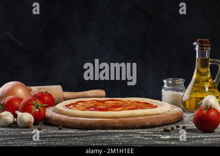 Pizza dough with sauce and other ingredients for making pizza on a black background. Stock Photo