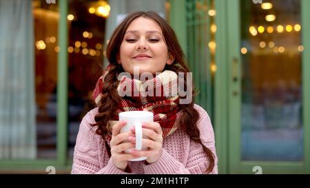 woman in checkered scarf drink hot coffee with marshmallow on street. holding hands with cup of cacao Stock Photo