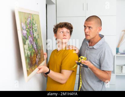 Son helps father to hang the painting on the wall of house Stock Photo