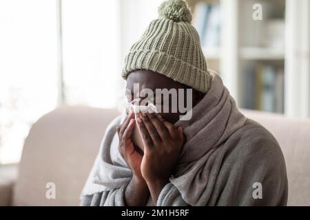 Unhappy black man feeling bad, blowing his nose at home Stock Photo
