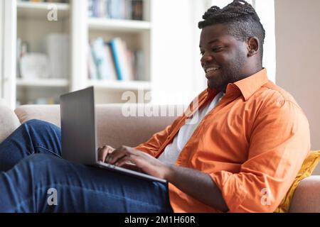 Happy Chubby Black Guy Using Laptop at Home Stock Photo